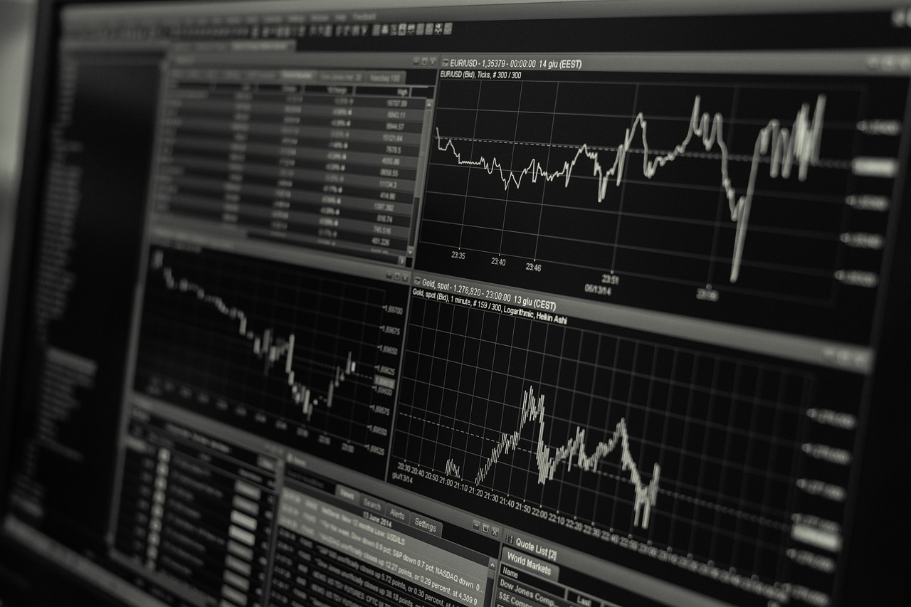 A black and white image of financial trading screens with stock market graphs and data displays.